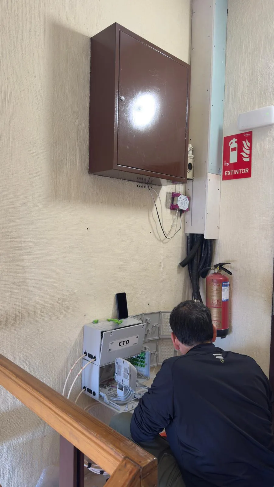 Técnico instalando y organizando CTO de fibra óptica en una zona común interior